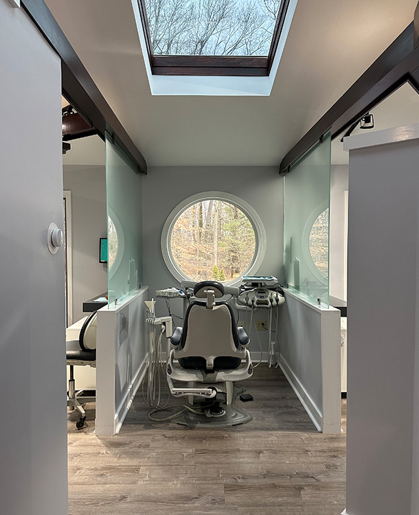 The image shows an interior space with a large window, a skylight, and a glass door leading to another room. There is a dental chair in the foreground, and the room appears to be a dental office or a similar professional setting.