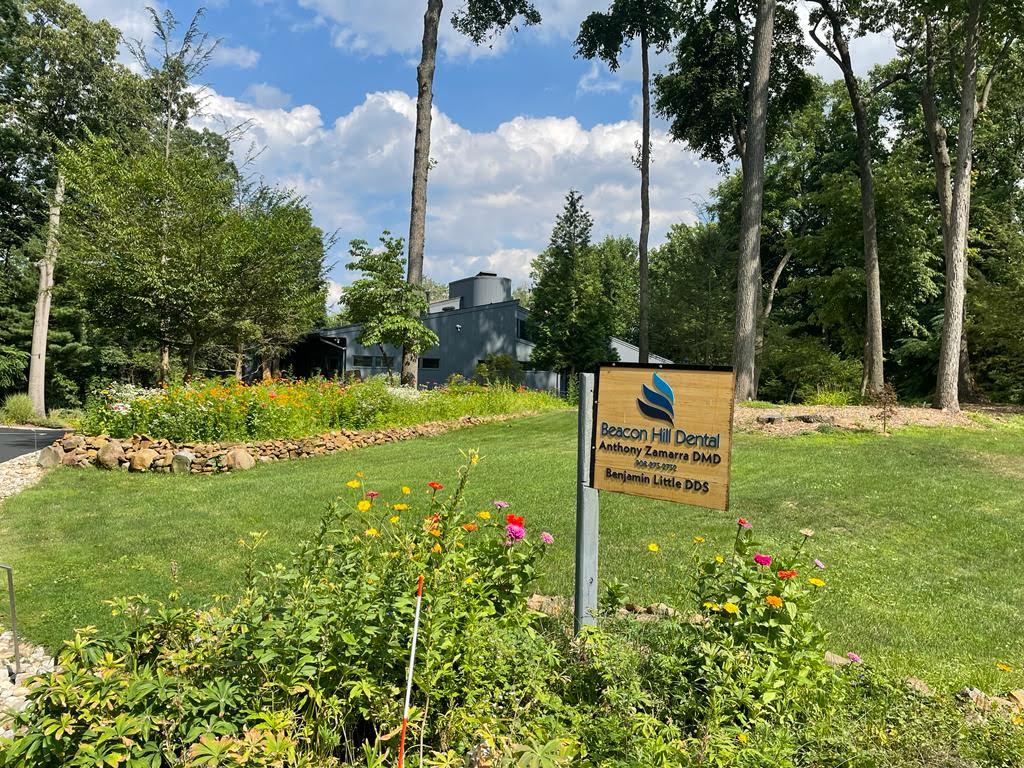 The image shows a sign in a grassy area with trees and a clear sky, indicating it is an outdoor setting.