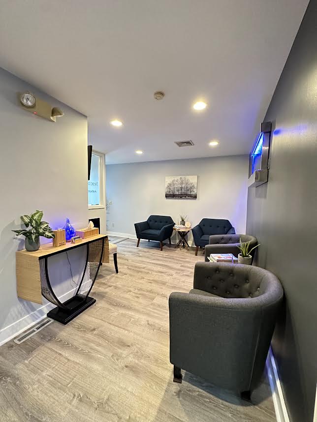 An interior view of a modern waiting room with a large open space, gray walls, and contemporary furniture.