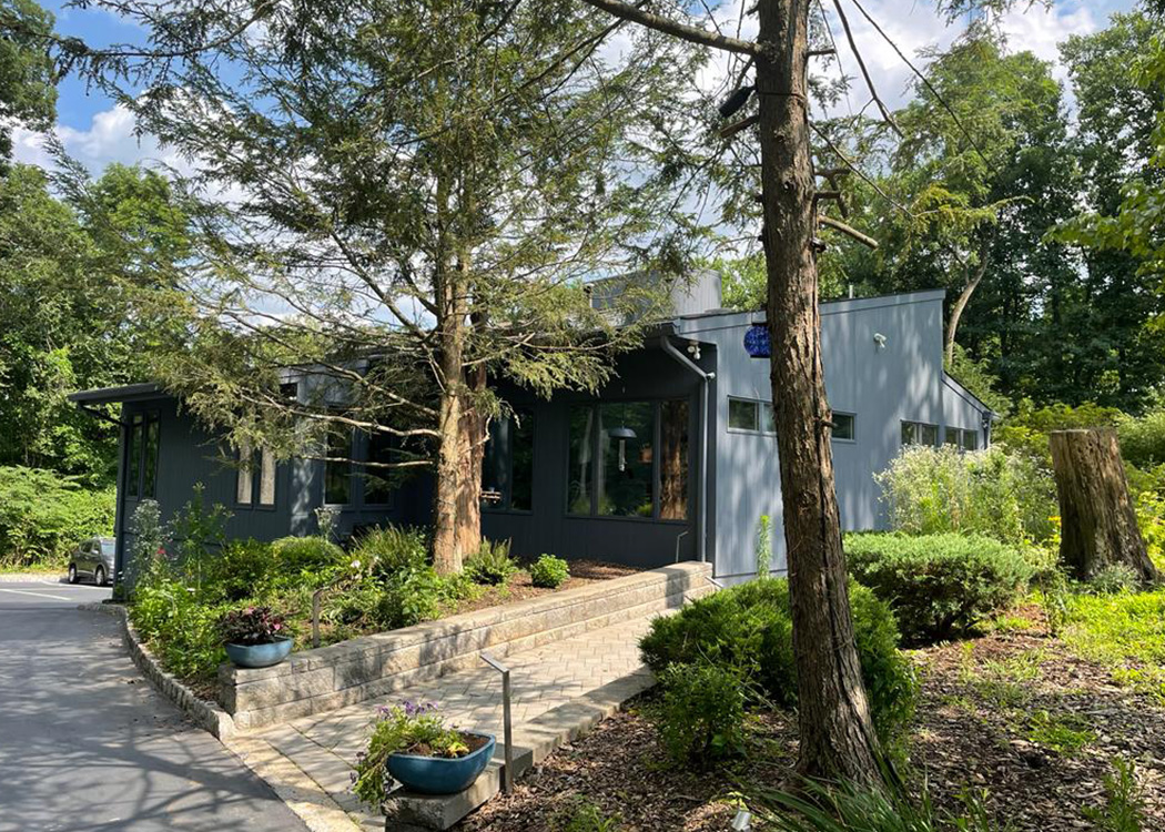 A modern, single-story house with a gray exterior and large windows, surrounded by well-maintained landscaping.