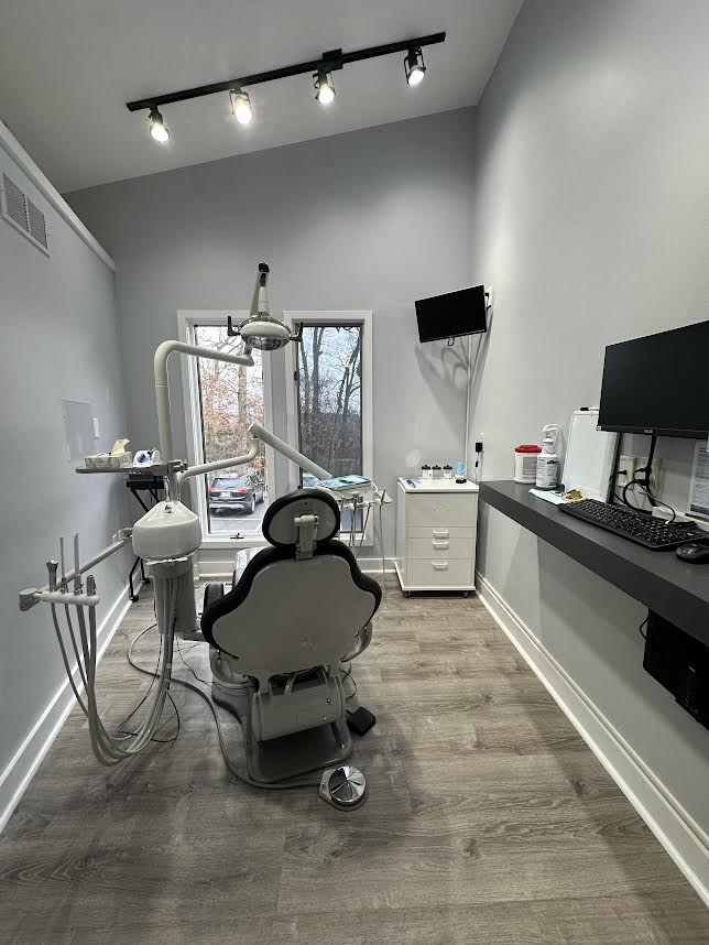 The image shows an interior view of a dental office with a chair, dental equipment, and a counter with a computer screen.