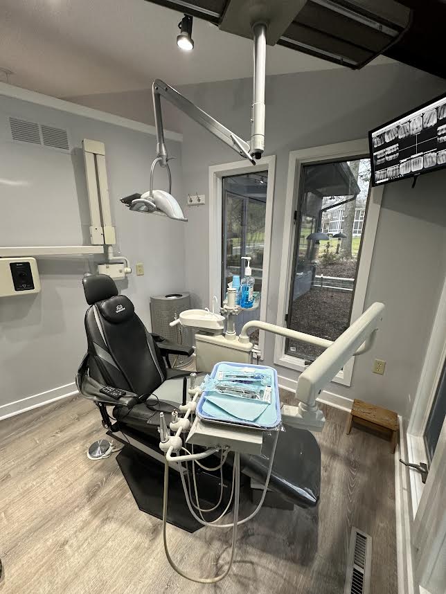 The image shows a dental office interior with a dental chair, examination table, and various dental equipment.