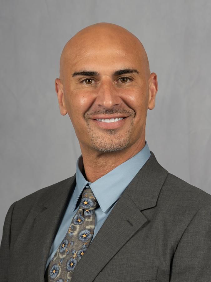 A man with a bald head, smiling at the camera, wearing a suit and tie.