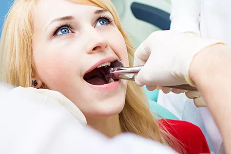 A woman in a dental chair receiving dental care, with a dentist using a drill on her teeth.