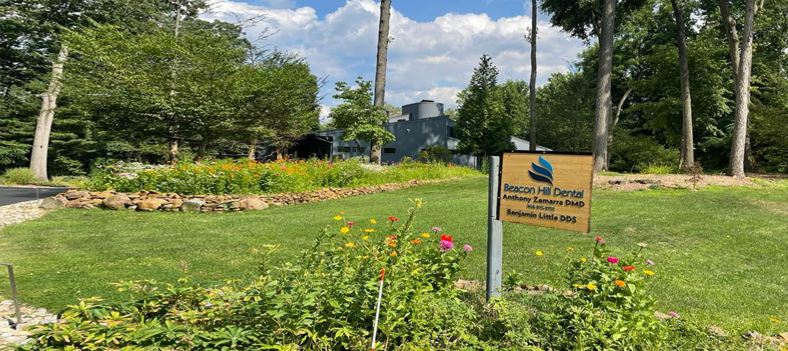 A sign in a park with a large expanse of grass and trees.