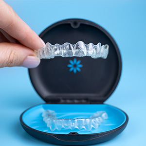 The image shows a person s hand holding an open package of dental braces, which are clear and consist of two arches with multiple brackets.