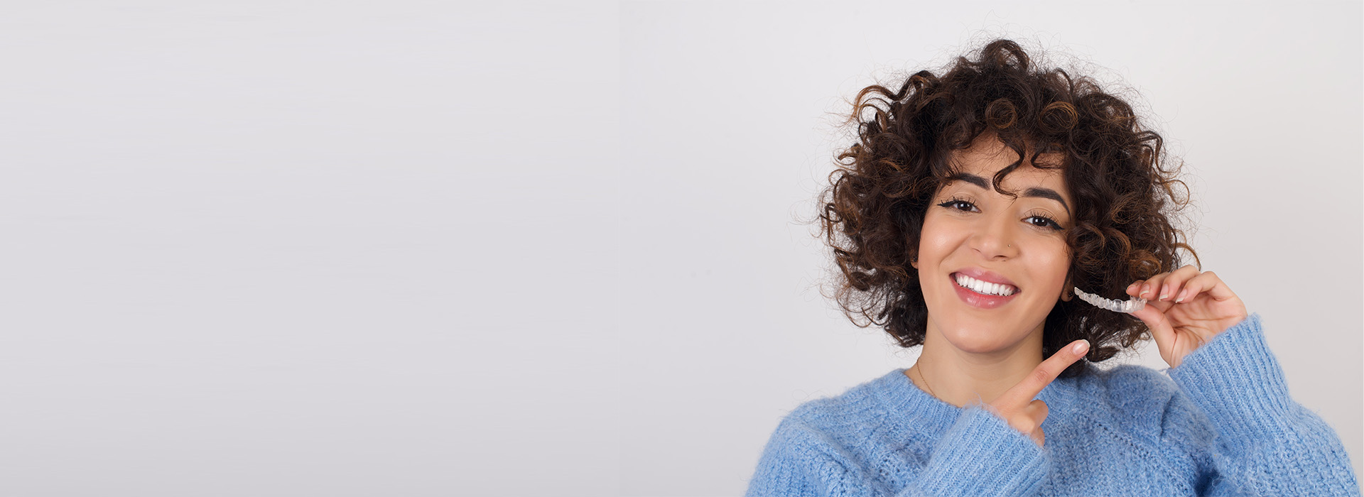 A woman with curly hair smiling at the camera, standing against a white background.