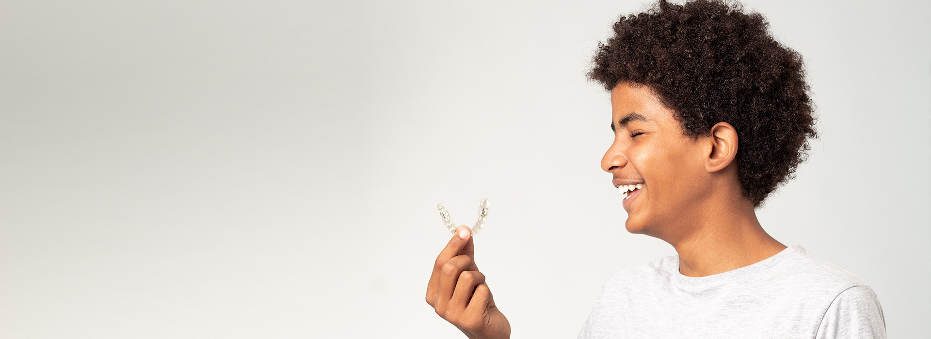 A smiling young man holds a small white flower, standing against a plain background.