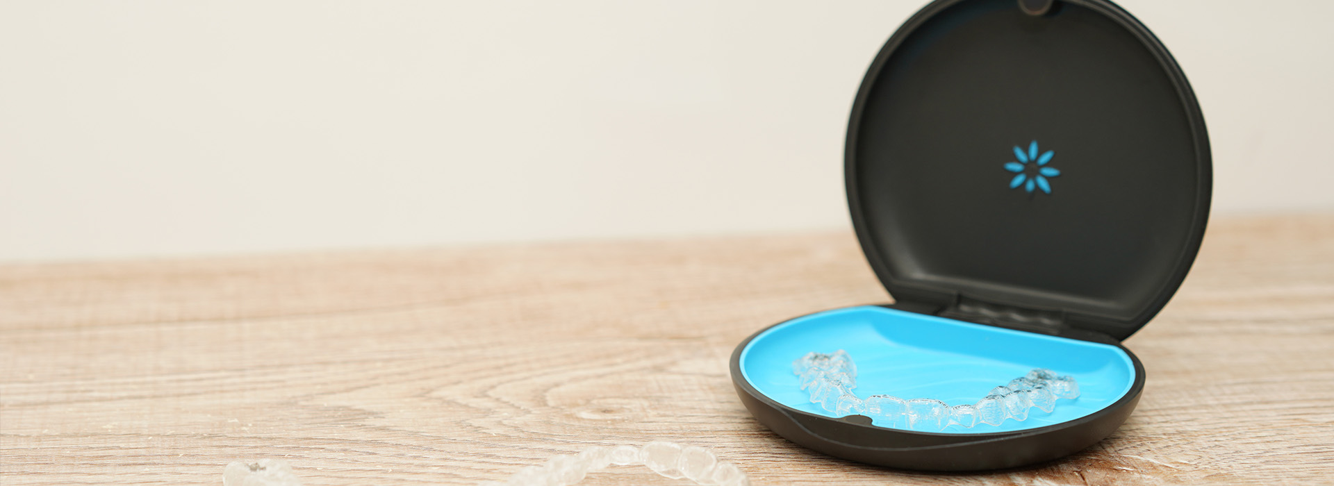 The image is a composite of two photos  the top photo shows a black smart device with a blue circular light on it, placed on a white surface. The bottom photo displays a close-up of a small blue object with a white label and a small white button on it, positioned against a dark background.