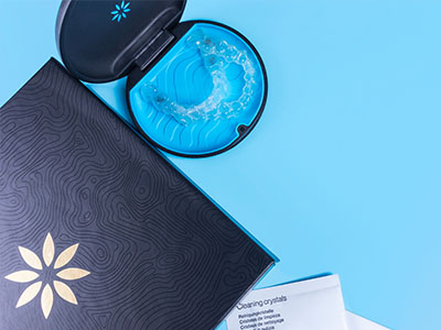 A product box with an open lid, revealing a dental appliance inside, placed against a blue background with a graphic design resembling a plant.