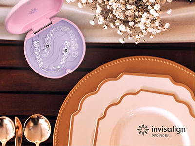 The image shows a collection of tableware including plates, bowls, and a spoon on a wooden surface, with a pink object that appears to be an eye care product in the foreground, and a toothbrush-shaped design on it.