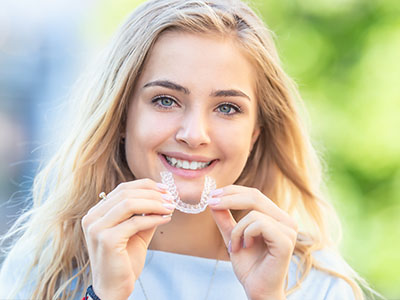 A young woman with a radiant smile, holding up a clear dental aligner.