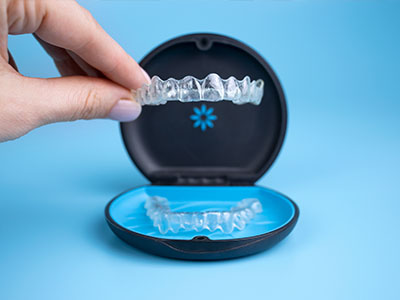 An image featuring a person s hand holding an open box containing a set of clear, plastic aligners, commonly used for teeth straightening.