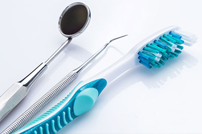 Dental tools, including a toothbrush with blue bristles and a pair of scissors, displayed on a white background.