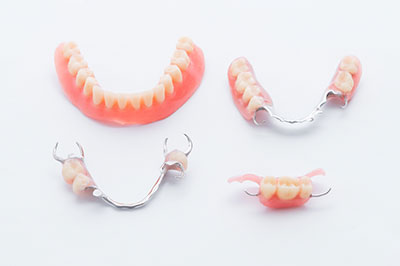 The image displays a collection of dental prosthetics, including a set of upper and lower dentures with teeth, and a single tooth with a metal clasp.