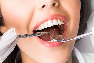 The image depicts a woman with an open mouth, receiving dental care from a professional using a dental tool.