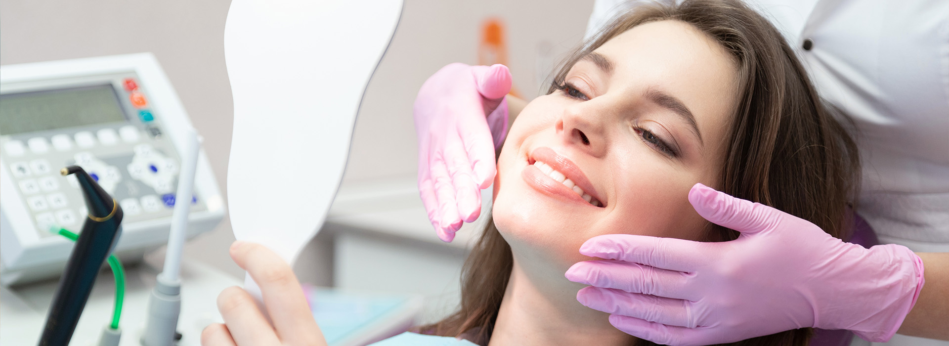 A woman receiving a dental cleaning, with a dentist holding a mirror to her face.