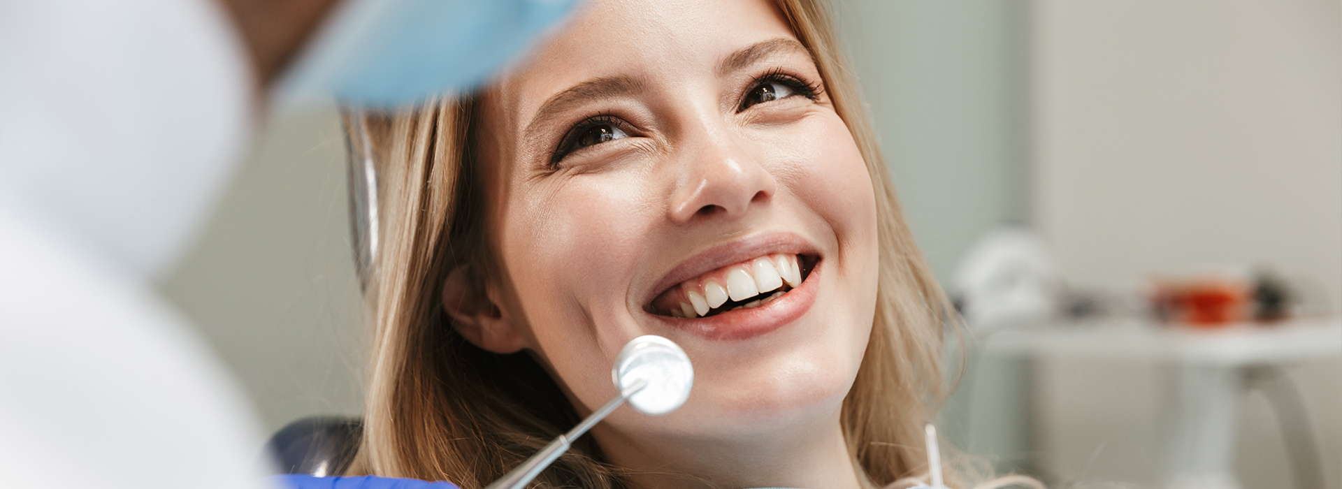 A smiling woman in a dental chair, receiving dental care from a professional.