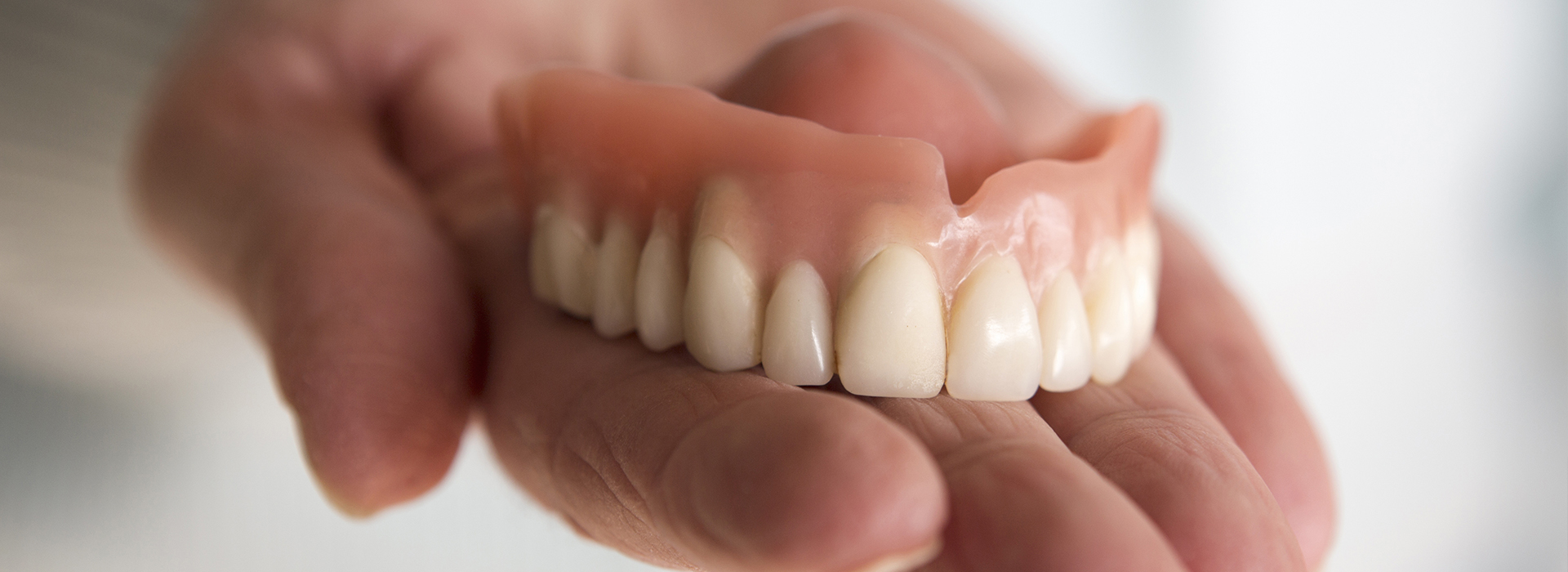 A hand holding a set of dentures against a white background.