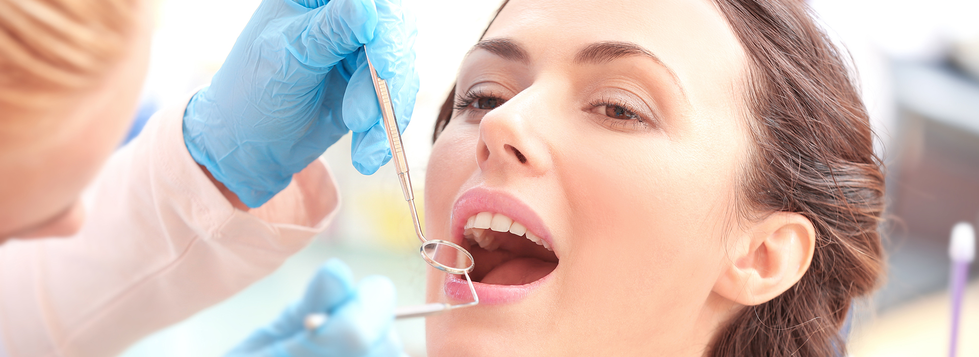 An image of a woman receiving dental care, with a dentist performing a procedure using a magnifying glass and dental tools.