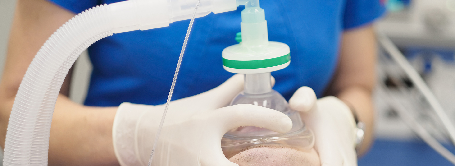 A person in a white lab coat and gloves is holding a clear plastic bag with a liquid inside, connected to a medical device, presumably in a laboratory setting.