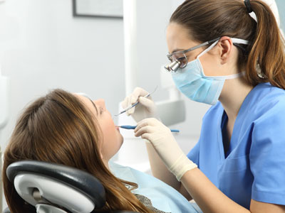 The image shows a dental hygienist performing a cleaning procedure on a patient s teeth while the patient is seated in a dental chair.