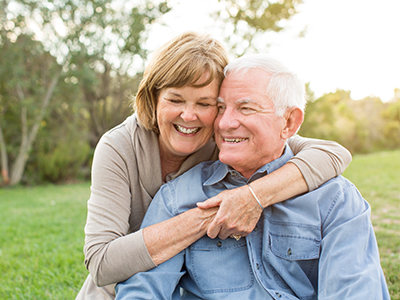 An elderly couple embracing and smiling in a park setting.