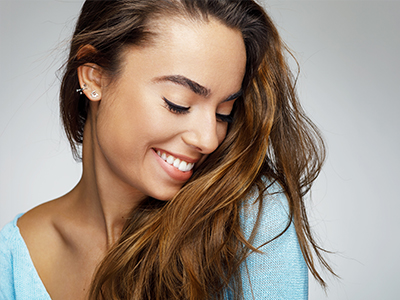 A woman with long hair smiling, set against a plain background.