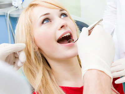 The image depicts a person in a dental chair receiving dental care, with a dentist performing an oral examination or procedure.