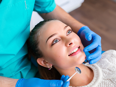 A dental hygienist performing a teeth cleaning procedure on a patient s mouth, with the patient smiling and looking towards the camera.