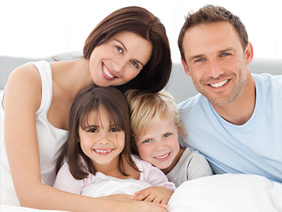 A family of five, including a man and woman with their three children, smiling together in bed.