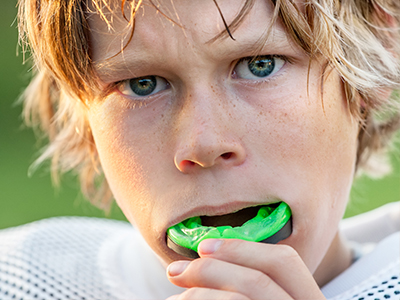 In the image, a young male with blonde hair and blue eyes is captured in a moment of playfulness, holding a green sports ball to his mouth as if it s a toothbrush.