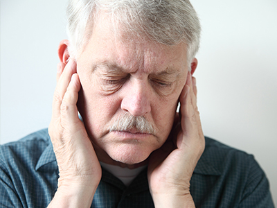 The image shows an elderly man with a mustache, holding his hand to his ear in a gesture of pain or discomfort.