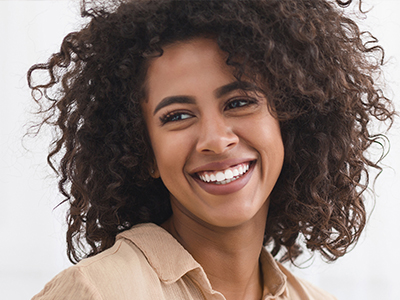 A woman with curly hair and a wide smile, wearing a beige top.